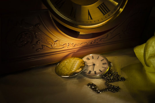 Old pocket watch in dark environment with old wall clock in background