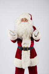 Santa Claus in eyeglasses and red costume throwing up hands on white background and looking into camera. American shot