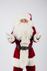 Santa Claus in eyeglasses and red costume throwing up hands on white background and looking into camera. American shot