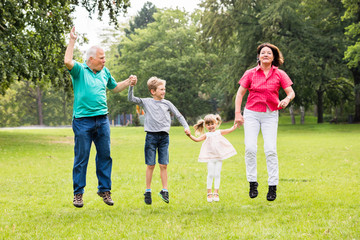 Obraz premium Grandparents And Grandchildren Jumping Together In Park