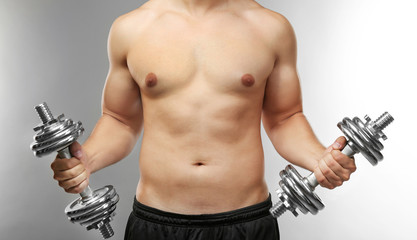 Sporty man with dumbbells on grey background
