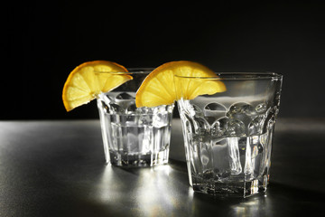 Glasses of vodka with lemon and ice on dark background