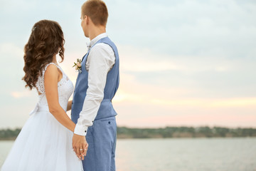 Beautiful wedding couple holding hands near river, close up view
