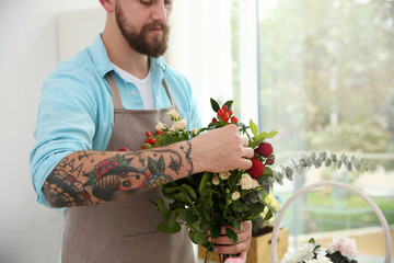Male tattooed florist holding bouquet of beautiful flowers, close up view