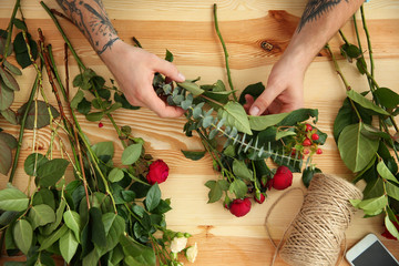 Close up view of tattooed florist preparing flower composition, on wooden background