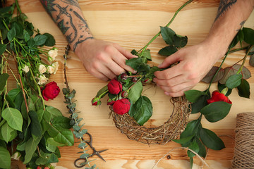 Close up view of tattooed florist preparing flower composition, on wooden background