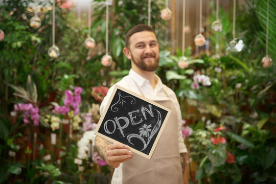 Handsome florist holding board with inscription OPEN