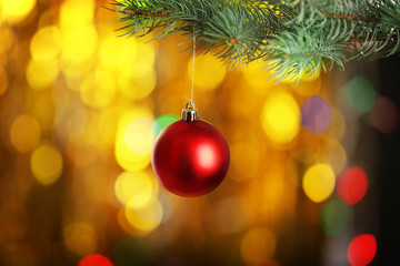 Fototapeta na wymiar Christmas ball hanging on fir tree branch on blurred golden lights background