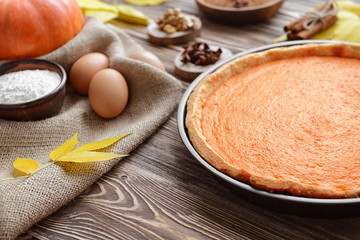 Delicious pumpkin cake in baking dish with ingredients on wooden background