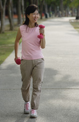 Mature woman using dumbbells, walking along path