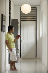 Man standing in hallway at home, holding a book, looking away