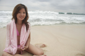 Fototapeta na wymiar Woman sitting on beach, smiling at camera