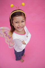 Young girl wearing fairy wings and deely bopper, arms crossed, smiling at camera