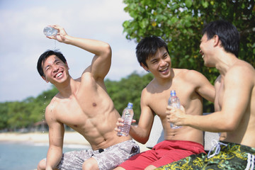 Three men sitting side by side, holding bottle of water