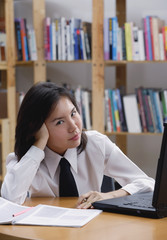 Young woman in library, leaning on hand, looking at camera