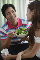 Couple talking, man eating a salad, woman holding a mug