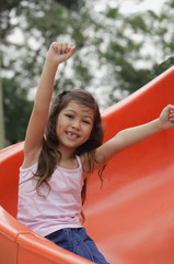 Girl coming down playground slide, arms outstretched
