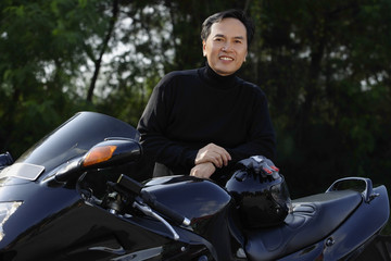 Fototapeta na wymiar Man standing by black motorcycle, smiling at camera