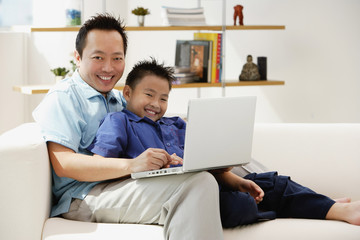 Father and son in living room with laptop, smiling at camera