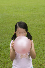 Girl standing on grass, blowing up pink balloon