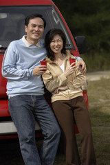 Man and woman leaning against red van, smiling at camera, camping