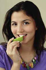 A teenage girl looks at the camera as she eats a piece of fruit