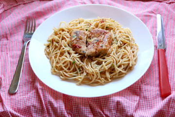 Chicken and pasta prepared with olive oil, tomatoes, parsley, garlic and butter. Checkered tablecloth, top view, selective focus.
