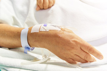 Fototapeta na wymiar Closeup saline water line at the hand of patient on bed in hospital room, infusion line in a patients hand
