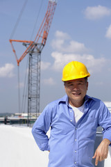 A man with a yellow helmet smiles at the camera as he works