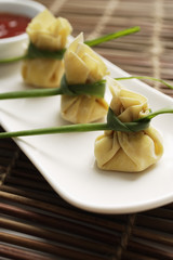 3 wanton dumplings placed in a row on a white plate with chili sauce on the side