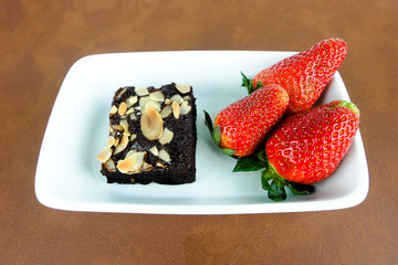 Brownie and fresh strawberry on white dish. 
