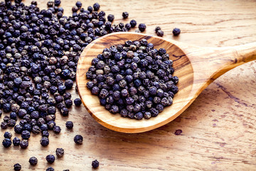 Closeup black pepper in wooden spoon on shabby teak wood table.