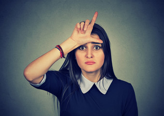 young unhappy woman giving loser sign on forehead