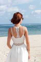 Fototapeta na wymiar back view of young woman in white dress on the tropical beach of Bali island, Indonesia. Ocean view.