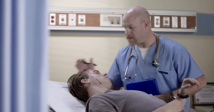 Male nurse enters examination room in hospital casualty department to care for young man with a serious head injury.  Recorded on fluid head tripod