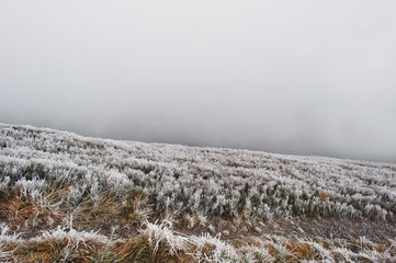 Mountainsides with frozen grass and fog on hill.
