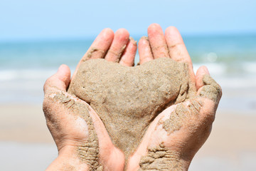 two hands holding sand in the shape of a heart