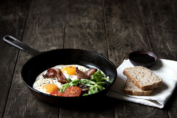 Breakfast set. Pan of fried eggs with bacon, tomato on wooden background
