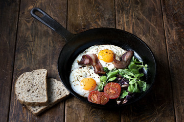 Breakfast set. Pan of fried eggs with bacon, tomato on wooden background