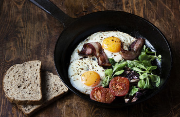 Breakfast set. Pan of fried eggs with bacon, tomato on wooden background