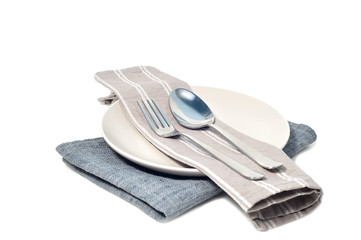 Gray napkin with stainless spoon and fork on white plate.