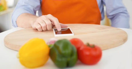 Closeup mid section of a mature man pointing finger to smartphone on the cutting board. Cooking, technology and home concept.