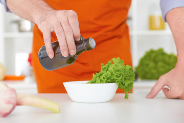 Food concept. Chef is pouring olive oil over fresh salad in restaurant kitchen.