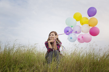 Beautiful girl sitting holding balloons in the prairie grass. On