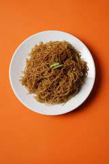 Noodles on plate on orange place mat.