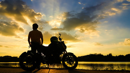 Fototapeta premium Silhouette biker with his motorbike beside the natural lake and beautiful twilight sky.