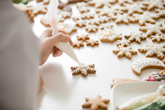 Close up of female confectioner hands decorating gingerbread stars with icing sugar using selfmade pastry bag, making decorative gingerbread ornaments