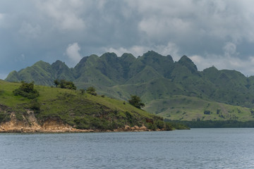 A small rock covered with green grass peeking from blue sea water on a background of blue hills (Singapore)