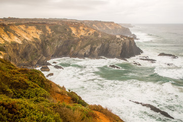 Fototapeta na wymiar Cliffs near the Atlantic ocean coast in cloudy rainy day in Alentejo, Portugal