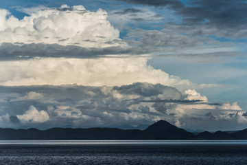 Menacing clouds and lovely clouds over the dark blue hills near the calm ocean (Singapore)